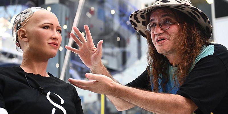 A co-founder of the project is pictured next to Sophia the robot, wearing a T-shirt with the SingularityNET logo.
